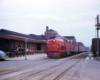 a diesel and passenger cars by a train station