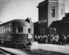 an observation car in front of a passenger depot filled with people waiting to board