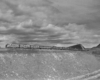 a diesel pulling passenger cars on a hill under a cloudy sky