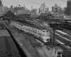 a diesel train pulling passenger cars with a train station in the background