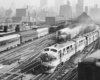 three passenger trains by a train station, with a the train in the foreground leaving the area