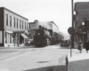 a steam engine pulling passenger cars through a small town downtown area