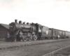 A black and white photo of a man approaching a train