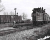 A black and white photo of a man standing by a stop light in front of a train