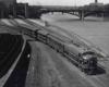 A black and white distant over head shot of a train next to a river