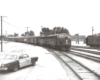 A black and white photo of a train parked on the tracks next to a taxi cab
