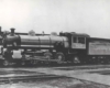 A black and white photo of a train parked outside a station