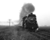 A black and white picture of locomotive 4-6-2 702 on the tracks with smoke coming out