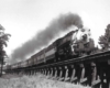 A black and white picture of locomotive 4-6-2 706 traveling down a raised railroad track with steam coming out of the chimney