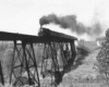 a stream engine passenger train on a tall bridge over a river