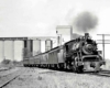 Steam locomotive with passenger on curve in front of silos