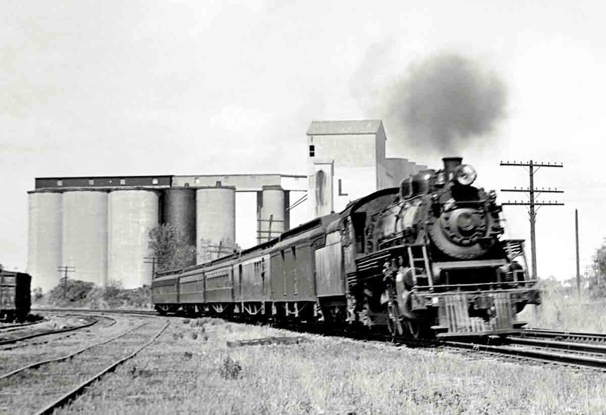 Steam locomotive with passenger on curve in front of silos