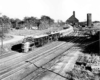 A black and white photo of a train passing through a lumber yard