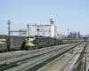 A yellow diesel locomotive pulling cars through a train yard