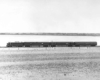 A black and white photo of a passenger train rolling through a flatland area
