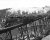 A steam engine and train on a tall wooden bridge