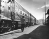 A black and white photo of a person walking by passenger cars