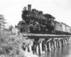 A black and white photo of a steam engine on a wooden bridge