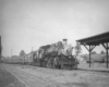 A black and white photo of a train parked outside a station