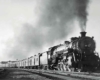 A black and white photo of a train approaching a station