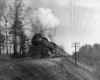 A black and white photo of a train traveling over a raised rail bed