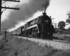 A black and white photo of a train passing through a rural town