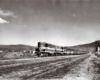 A black and white distant shot of a train passing through a rural area