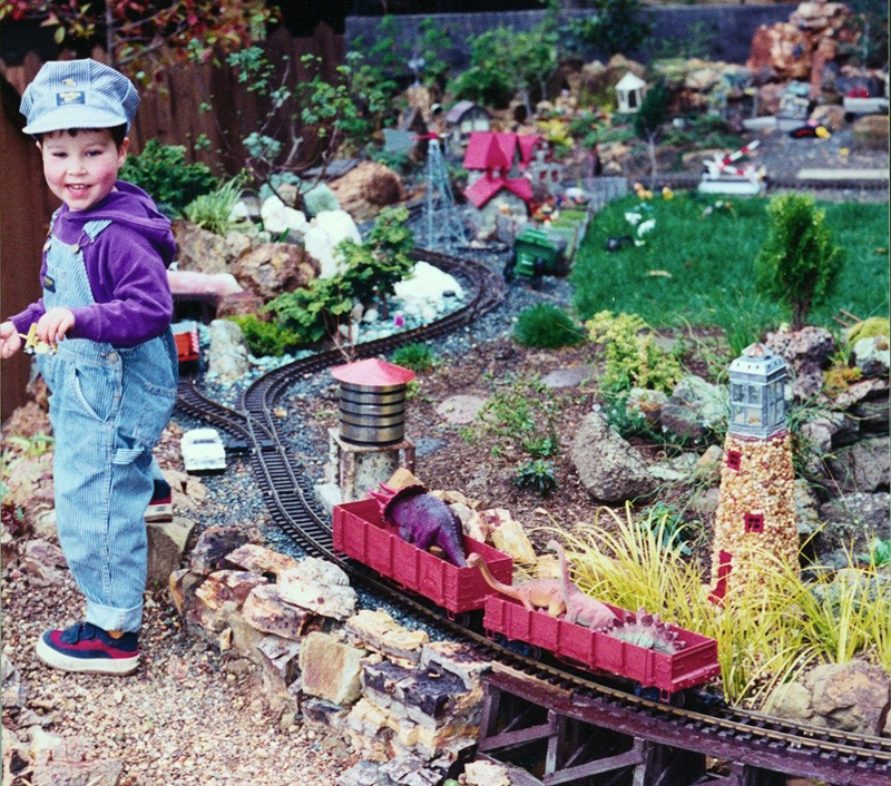child in engineer's outfit near garden railway