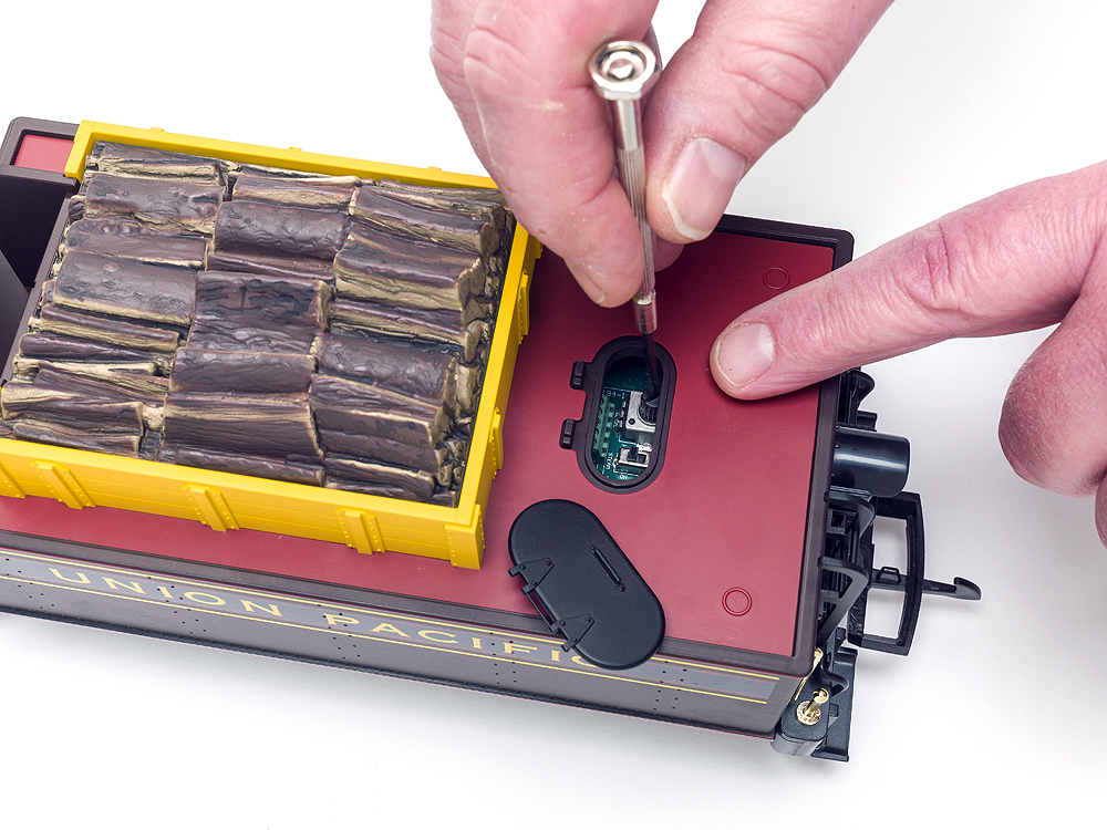 Top view of Piko mogul's tender and two hands over an open hatch, one holding a screwdriver. The tender holds the DCC circuit board.