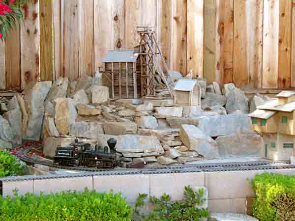 rocky scene on garden railroad with black engine and fence in the background