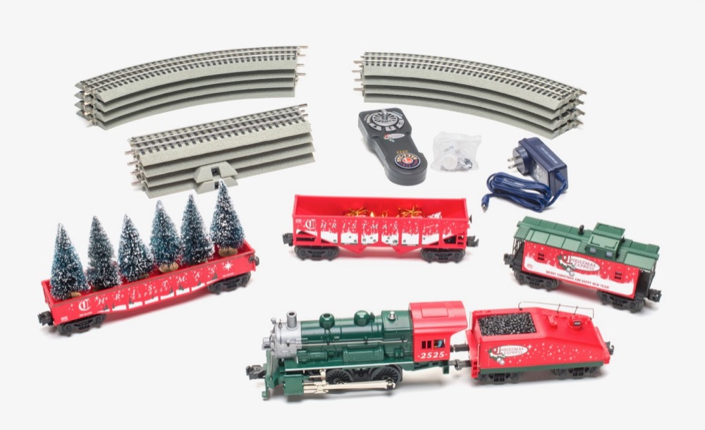 Component pieces of the LionChief Christmas Express set: Gondola with Christmas trees, hopper, caboose, 0-4-0 locomotive, power controller and wires, curved and straight track sections.