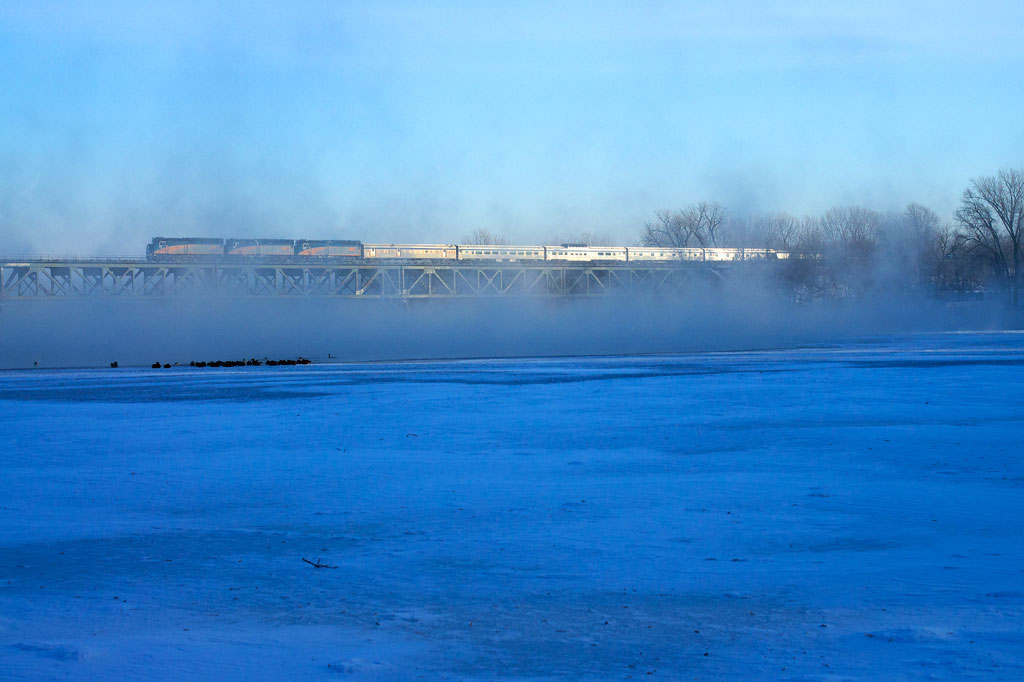 A distant shot of a train traveling over a snowy and icy bridge