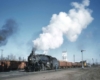 A train passing by with big white smoke coming out of its chimney