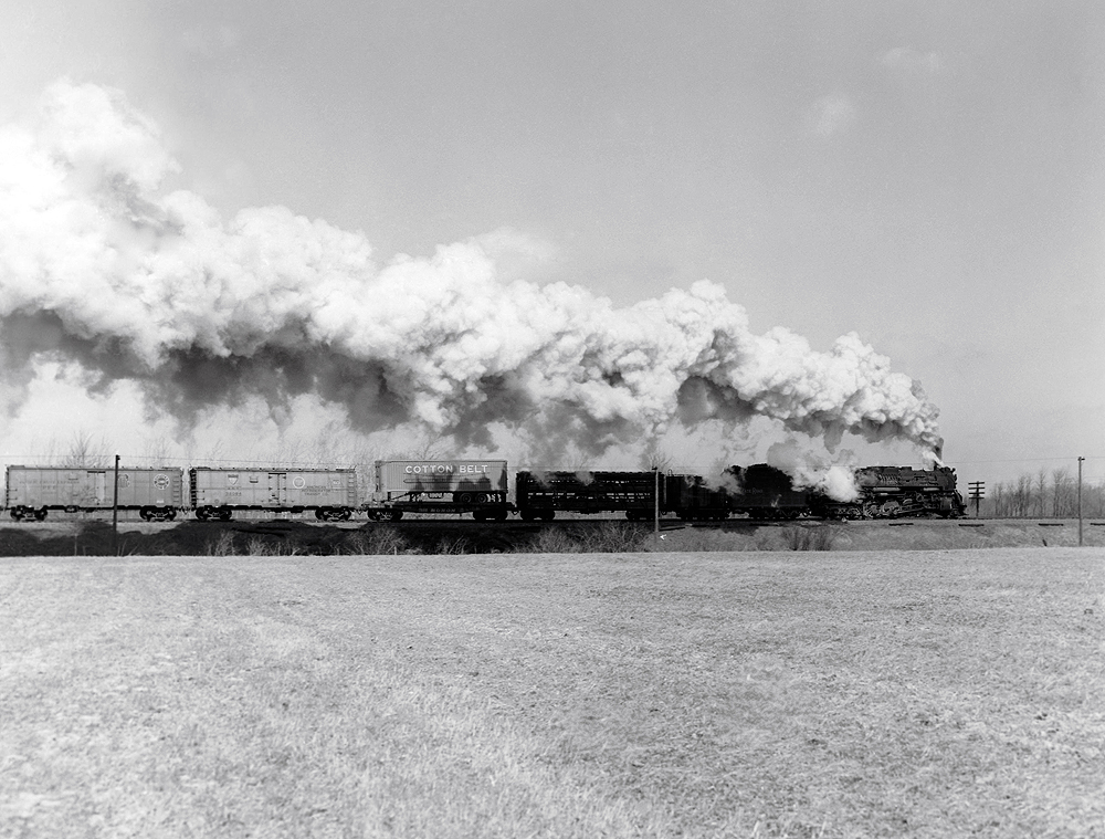 A distant shot of a train passing by with big white smoke coming out of its chimney