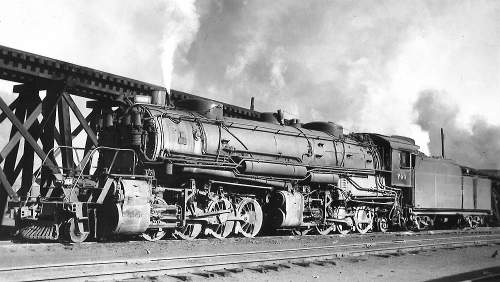 A train passing by with white smoke coming out of its chimney