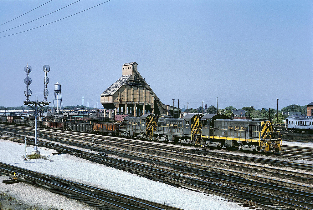 A yellow and black train passing by a coaling tower