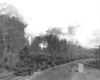 A black and white picture of someone standing on the side of the tracks watching 2-8-8-2 Mallet 740 move down the tracks with smoke coming out of its chimney