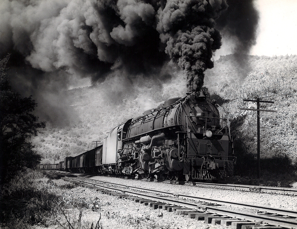 A black and white photo of locomotive 4-6-6-4 661 coming down the tracks with big black smoke coming out of its chimney