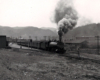 A black and white photo of Clinchfield 4-6-2 with smoke coming out of the chimney passing through buildings