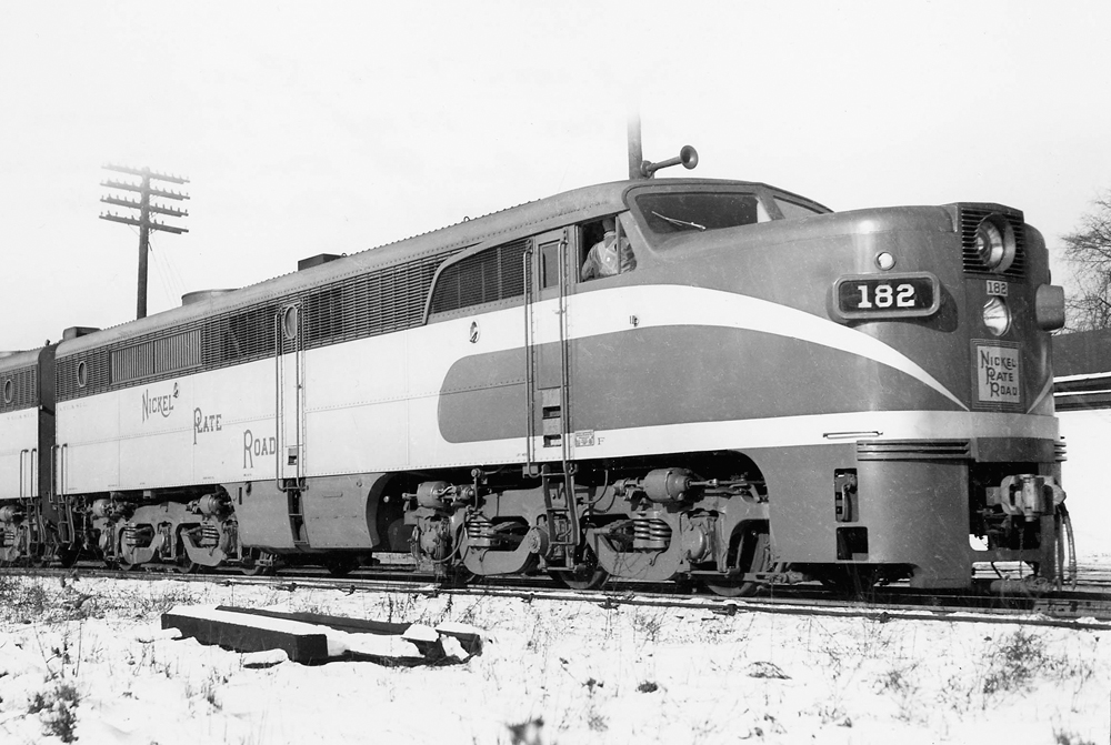 A black and white close up photo of Nickel Plate’s 11 Alco with the conductor inside the train