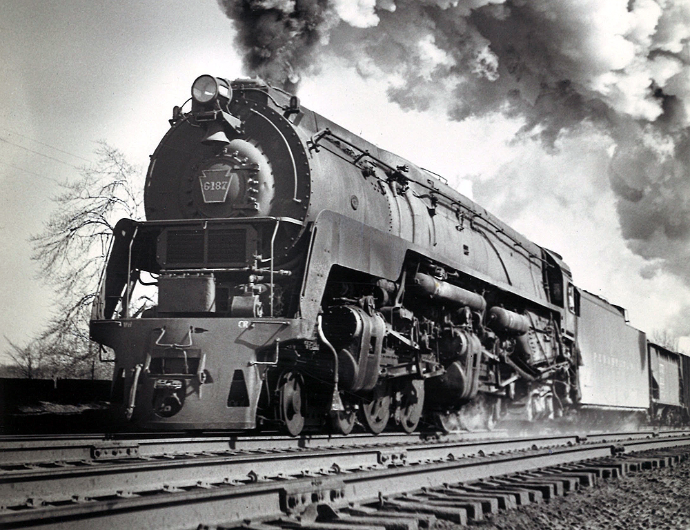 A close up black and white photo of a Q2 6187 locomotive coming own the tracks with big smoke coming out of its chimney