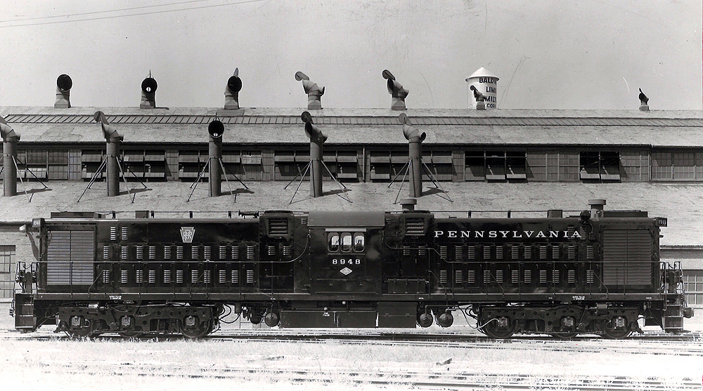 A black and white full length picture of a Lima-Hamilton 2,500 h.p. twin-engine transfer unit No. 8948 locomotive in front of a building