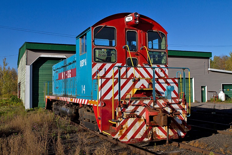 A red and white train parked outside an enginehouse