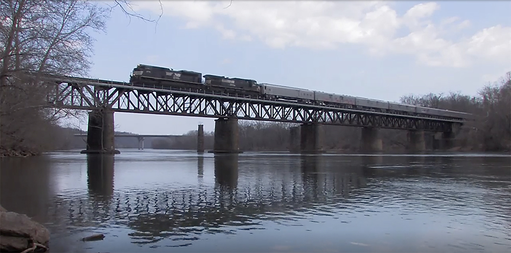 Blue and yellow-painted locomotives lead a circus train on a bridge over a river.