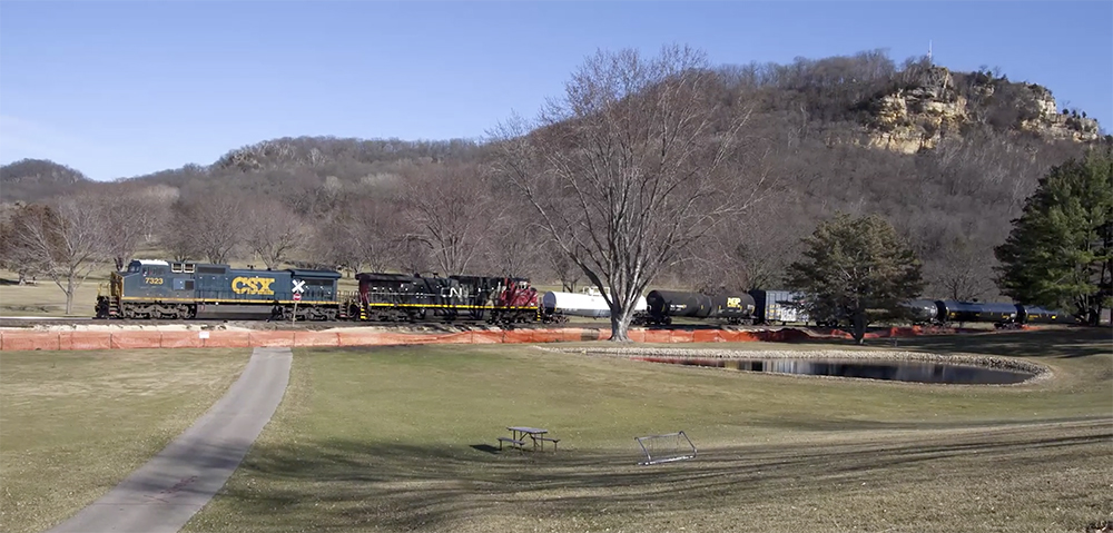 A blue-painted locomotive leads a freight train in rolling terrain under blue skies.