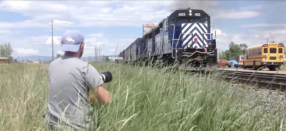 Drew Halverson looks on at a blue and white-stripped Montana Rail Link diesel locomotive.