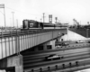 a gt passenger train on an overpass with a six lane highway underneath