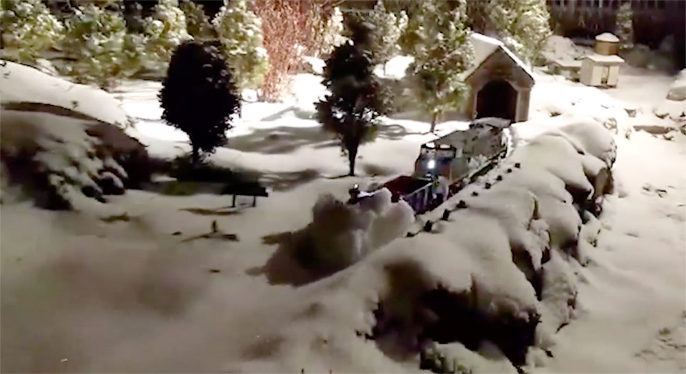 plow clearing snow off of garden railroad tracks at night