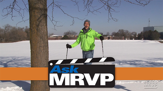 David Popp wearing a winter hat, bright yellow jacket, and cross country skis outside in the snow.