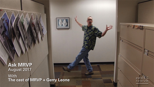 David Popp walking by a hallway entrance with his hands in the air and making a silly face.